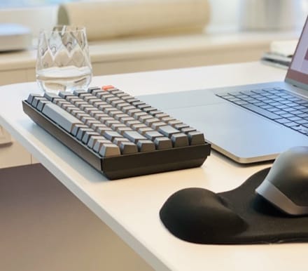 Typemaster keyboard, from the right side, in front of a laopt, on top of a work surface with a glass and mousepad