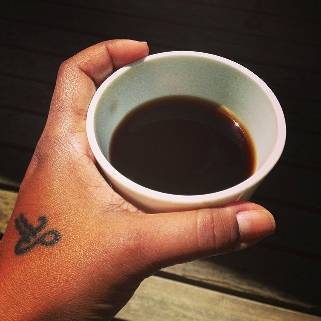 Close up photo of a hand holding a cup about three-quarters filled with a dark liquid, presumably coffee.